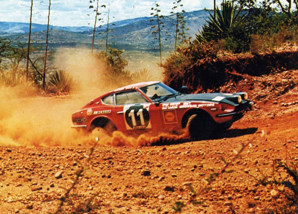 The liveried red-and-black 1971 Datsun 240Z East African Safari Rally car drifting around a dirt hill corner