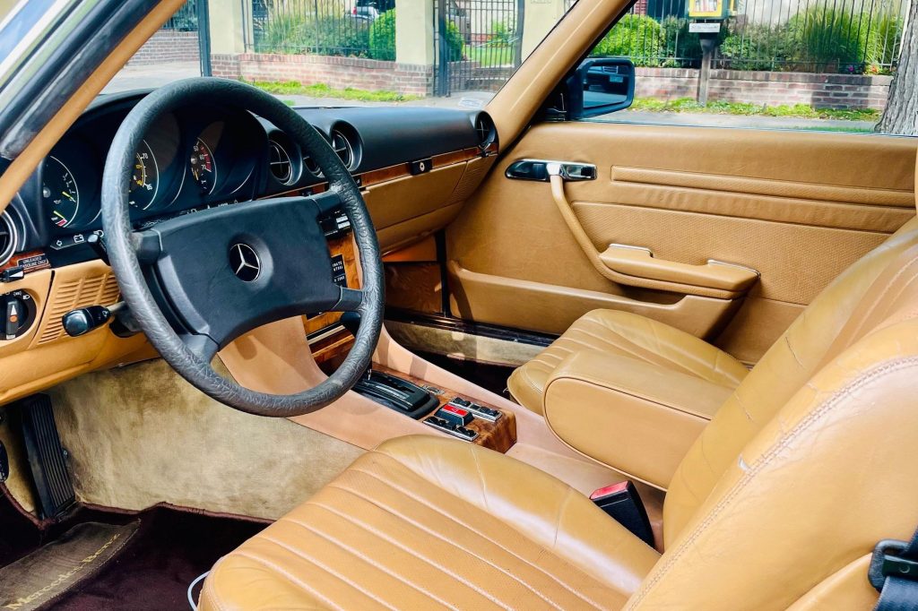 The tan-leather-upholstered front seats and wood-trimmed black dashboard of a 1981 C107 Mercedes 380 SLC