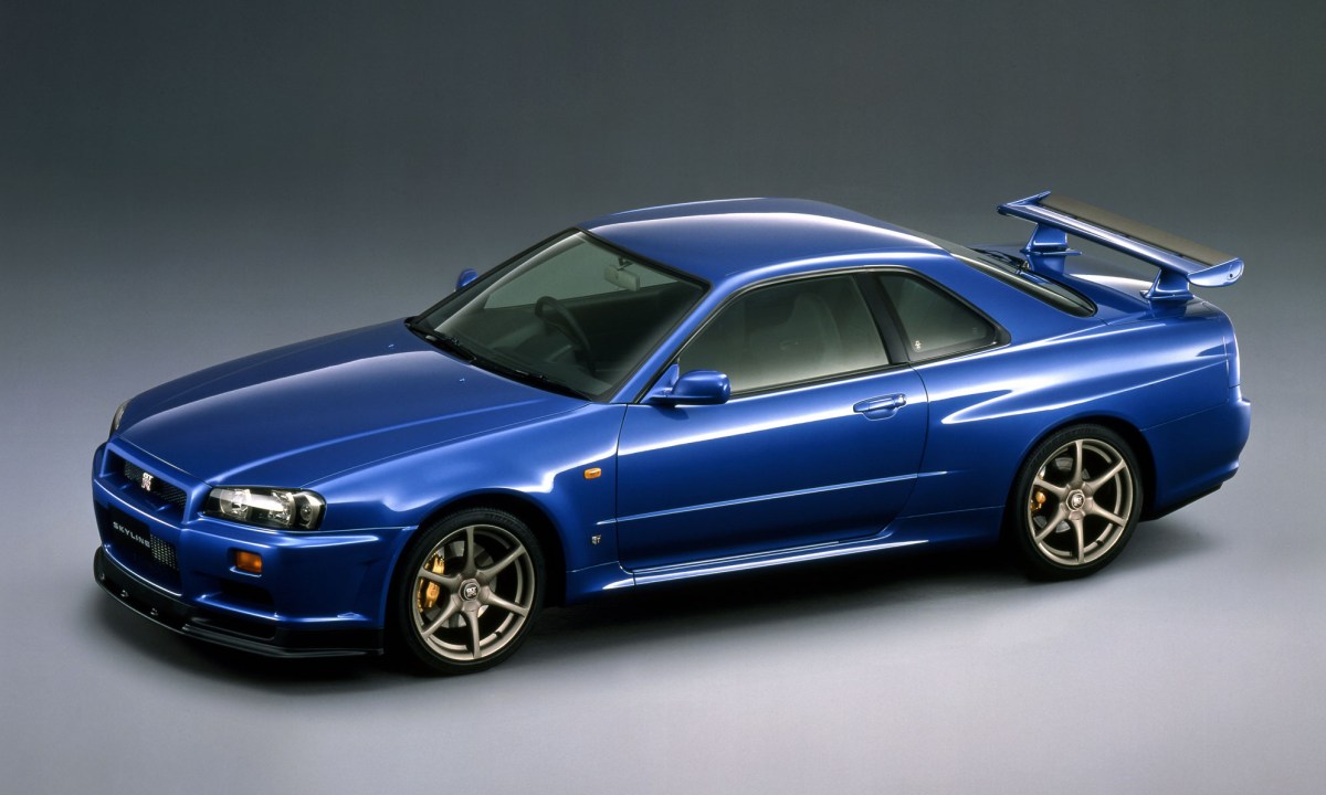 A blue 1999 Nissan R34 GT-R Vspec photographed in a studio with a grey background