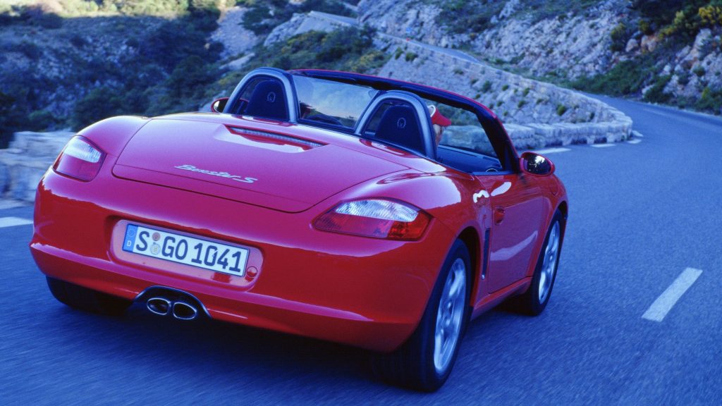The rear 3/4 view of a red 2005 Porsche Boxster S driving around a mountain road