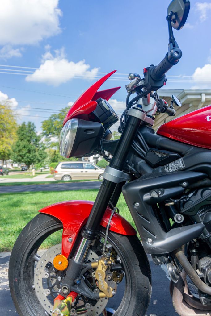 The side view of the black adjustable fork on a red-and-black 2012 Triumph Street Triple R motorcycle