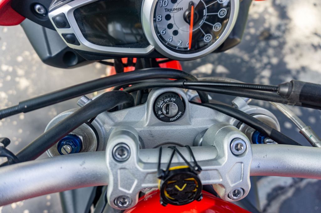 An overhead view of the blue preload adjusters and silver rebound damping adjusters on top of a red 2012 Triumph Street Triple R motorcycle's forks