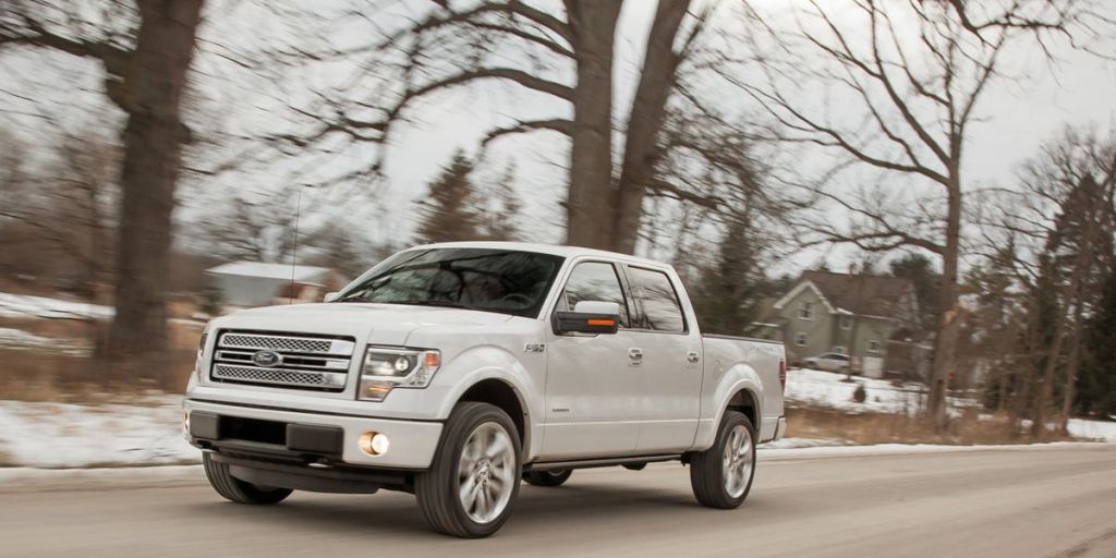 a white 2013 Ford F-150 drives on a road in the snow