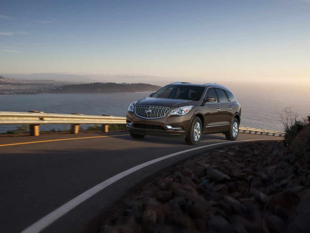 A brown 2015 Buick Enclave drives around a large bend in the road, in 2021 it's a great option for a used midsize SUV.