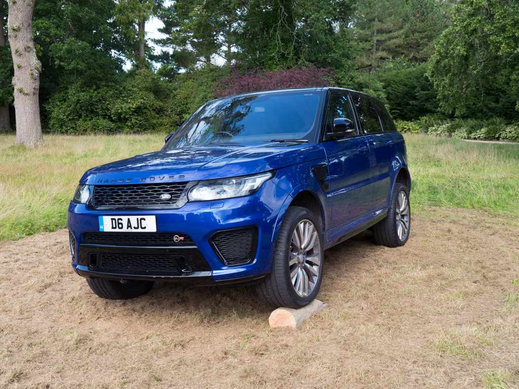 A blue 2017 Range Rover sport parked outside with one wheel up, its the most recent generation of Range Rover.