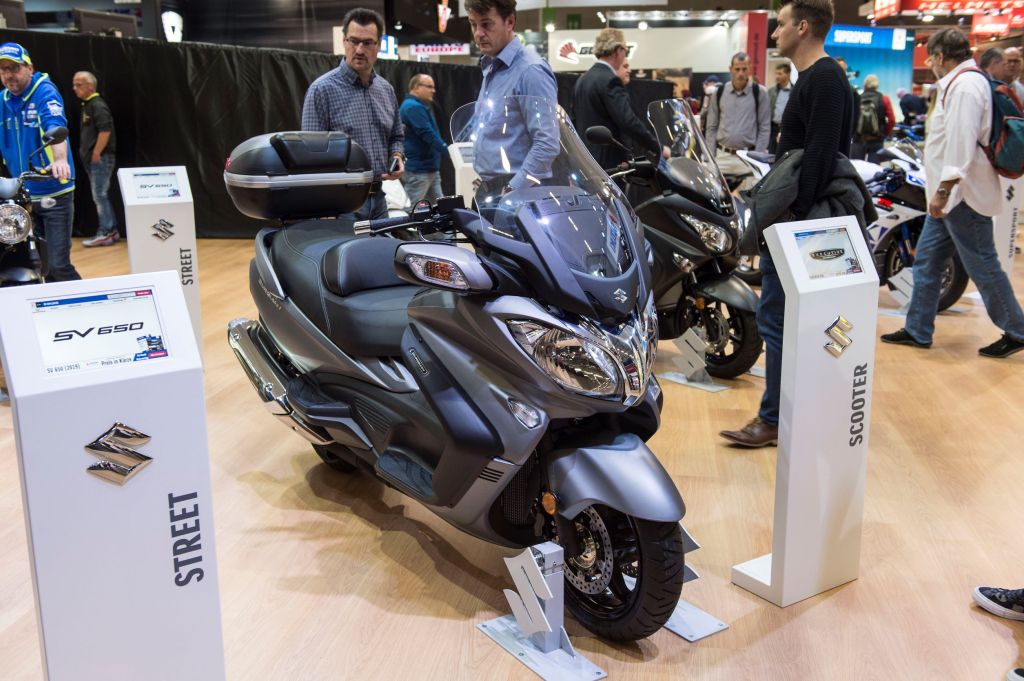 Intermot Trade Fair goers look at a gray 2018 Suzuki Burgman 650 Executive scooter