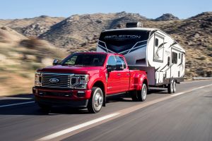 The 2020 Ford F-350 Platinum F-Series Super Duty pickup truck in red towing an RV motor home on a country highway