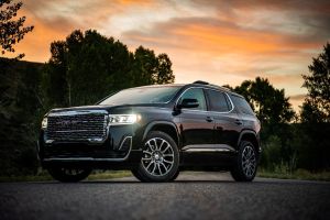 The 2020 GMC Acadia Denali midsize SUV parked at sunset with its headlights on