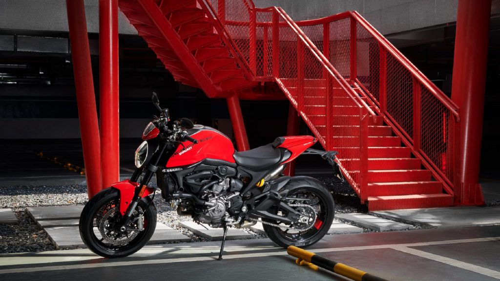 A red-and-black 2021 Ducati Monster Plus parked by a red metal staircase