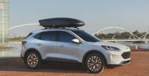 The 2021 Ford Escape SE compact SUV in white parked on a dirt beach near a river and bridge