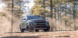 The 2021 Ford Explorer Timberline midsize crossover SUV in dark green parked in the middle of a forest and surrounded by sparse trees
