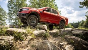 The 2021 Ford Ranger Tremor Lariat light pickup truck in red parked atop a hill of uneven terrain and rocks