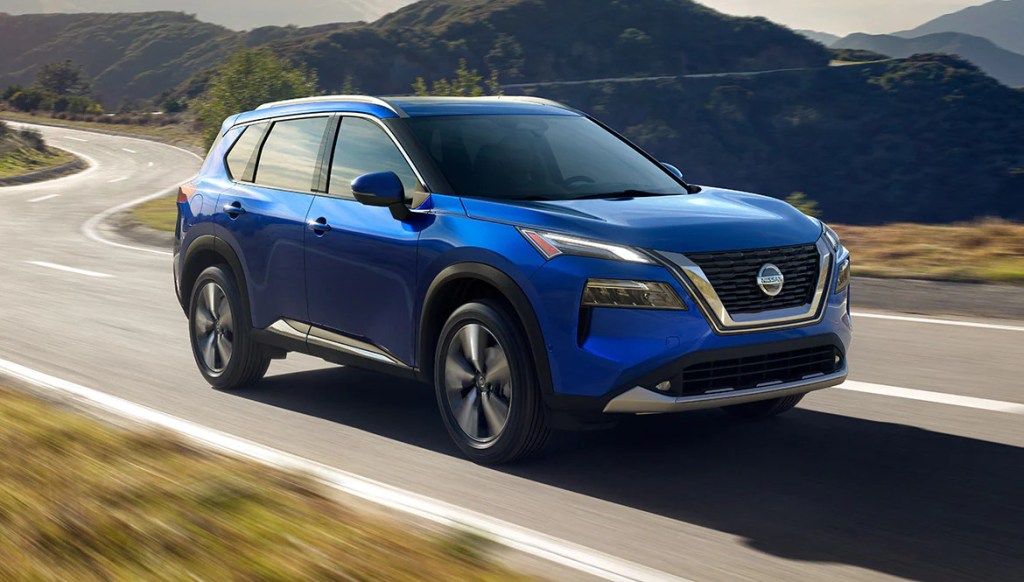 A blue 2021 Nissan Rogue drives on a road
