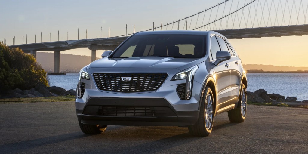 A silver Cadillac XT4 parked in front of a bridge at sunset. 