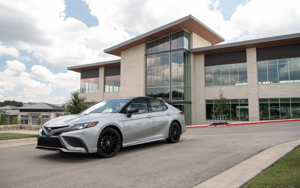 A 2021 Toyota Camry Hybrid XSE in silver sitting in front a nice futuristic building.