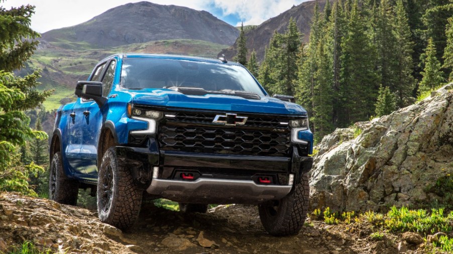 The 2022 Chevrolet Silverado ZR2 pick up truck painted in light blue driving towards the camera on a mountain path with lush green trees behind it. General Motors has just begun shipping out trucks again after production was paused due to the global semiconductor shortage