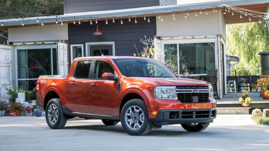 The 2022 Ford Maverick Lariat compact pickup truck in orange red parked outside of a house and patio