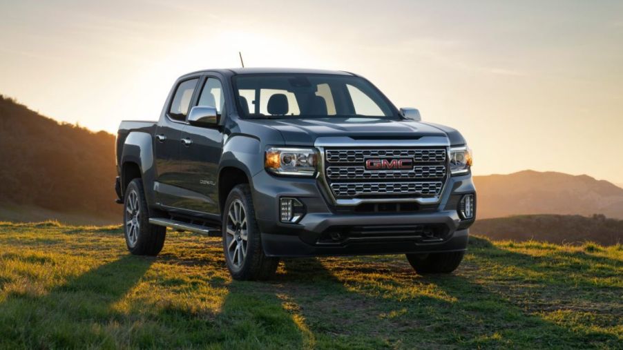 The 2022 GMC Canyon midsize pickup truck parked on a grass field as the sun sets on rolling hills