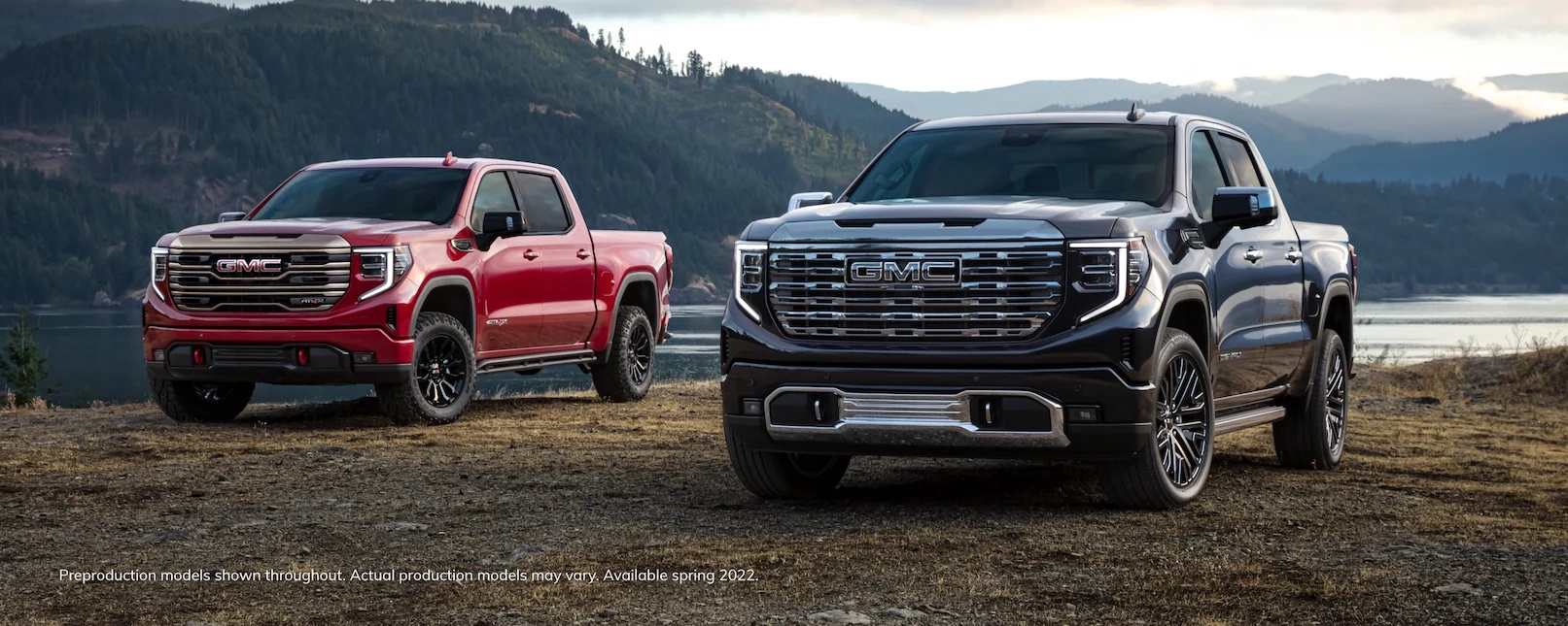 A red and a dark blue 2022 GMC Sierra 1500 parked in front of a lake.