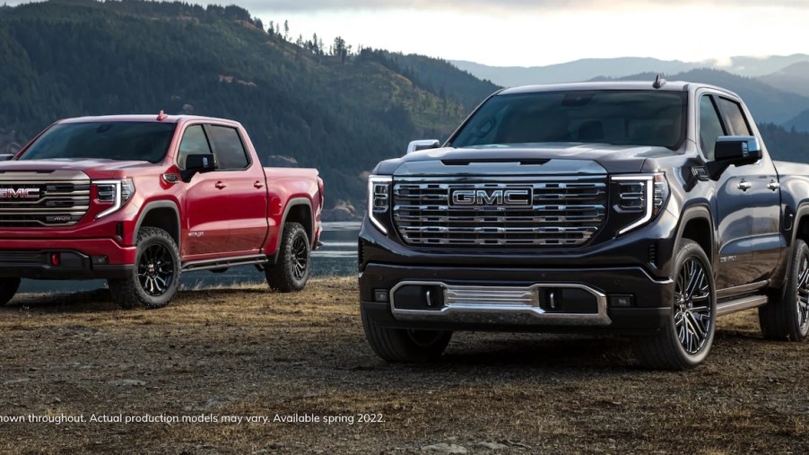 A red and a dark blue 2022 GMC Sierra 1500 parked in front of a lake.