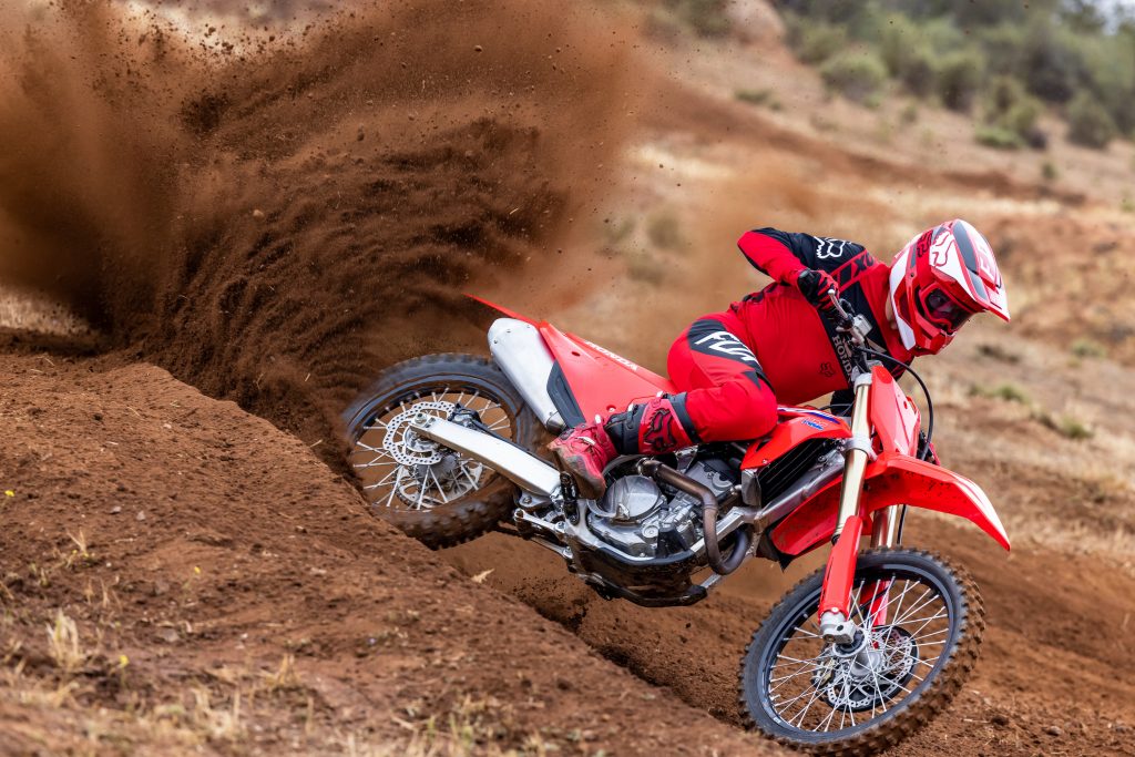 A red-clad rider slides a red 2022 Honda CRF250R dirt bike through the dirt