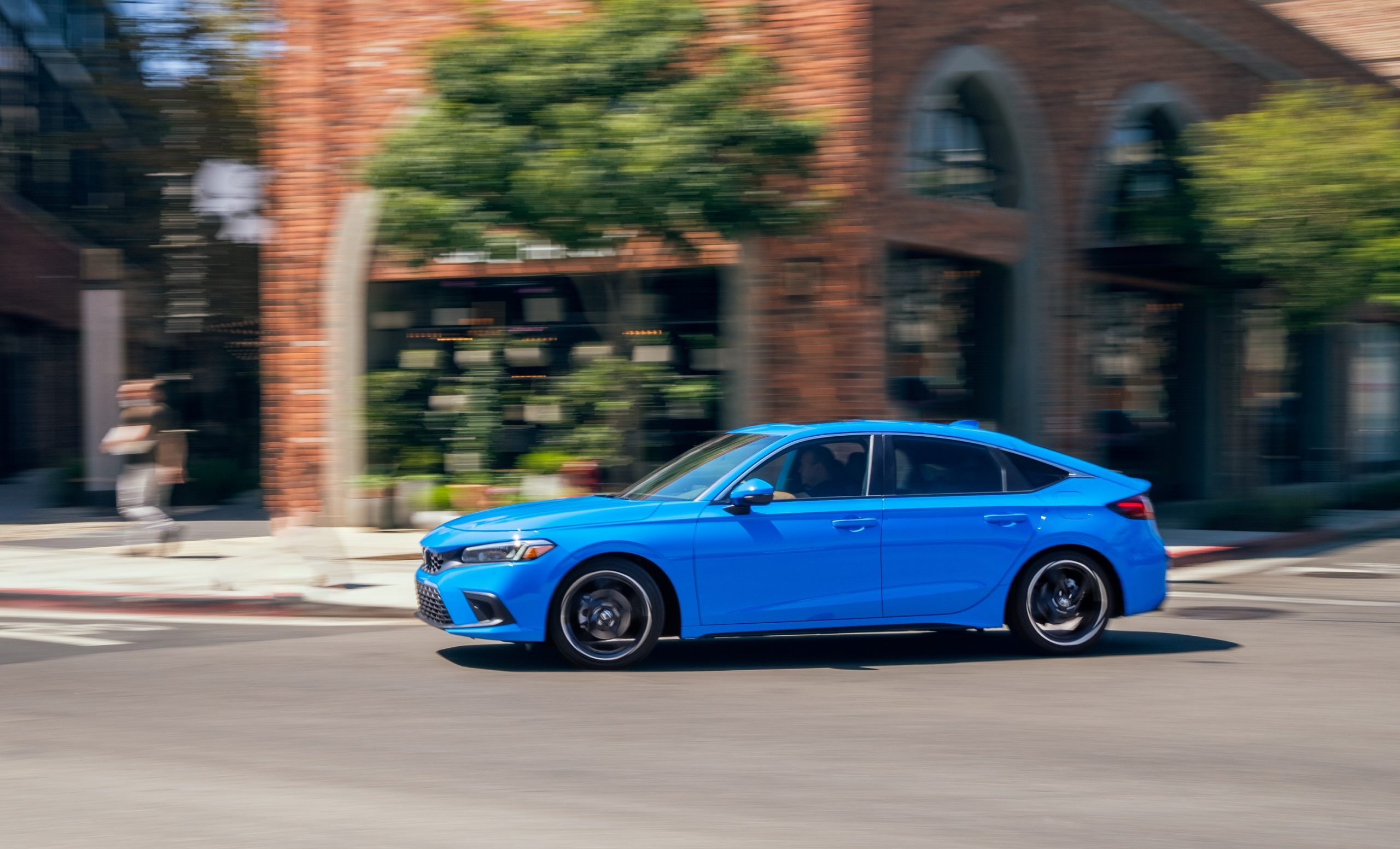 A blue 2022 Honda Civic hatchback shot in profile while rolling down a city street