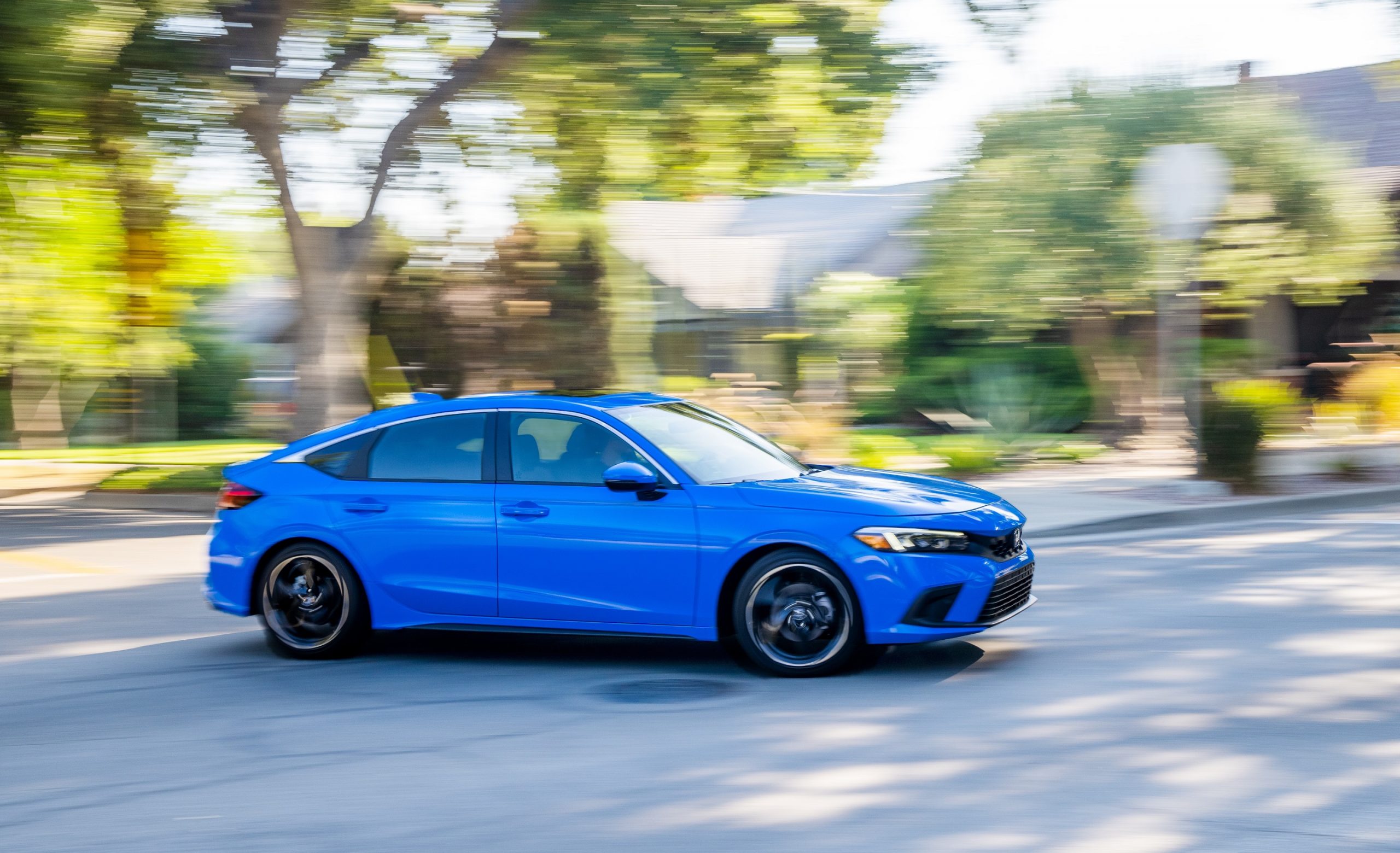 A blue 2022 Honda Civic hatchback shot in profile on a shaded street