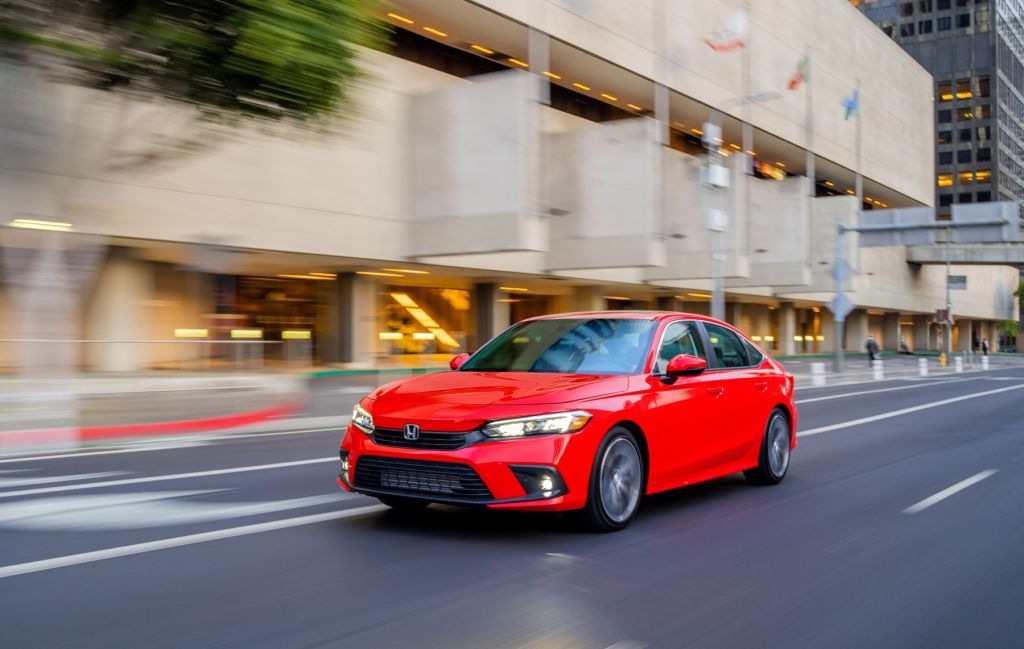 The 2022 Honda Civic Touring Sedan in red driving through a city as one of the best cheapest new sedans in our buyers guide