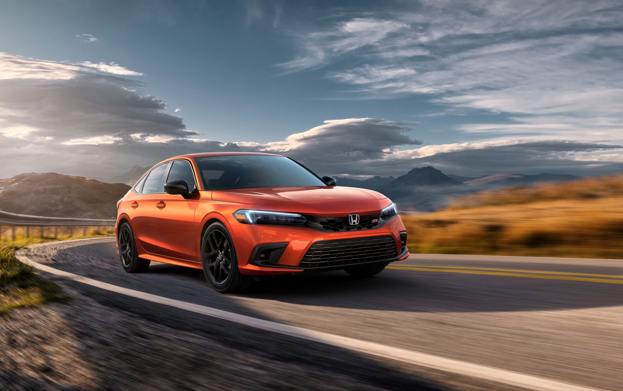 An orange 2022 Honda Civic Si shot from the front 3/4 on a mountain pass