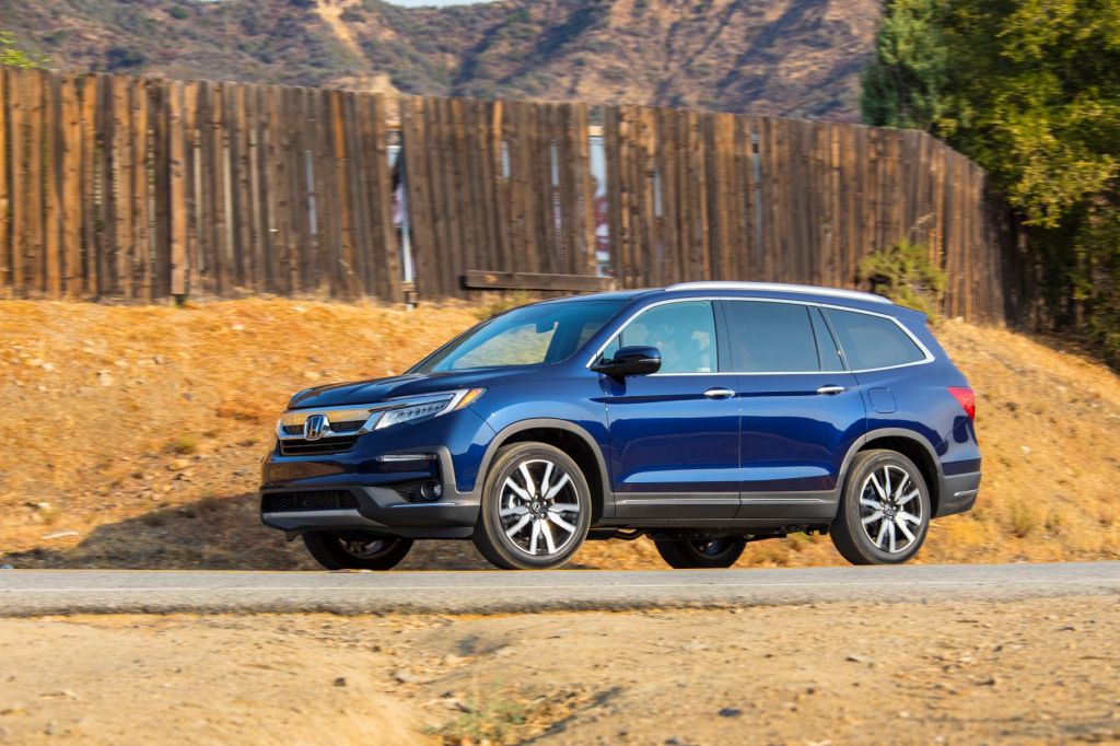 The 2022 Honda Pilot Elite SUV in blue parked in the desert near a wooden fence, Honda killed the LX and EX Pilot trims for the new model year.