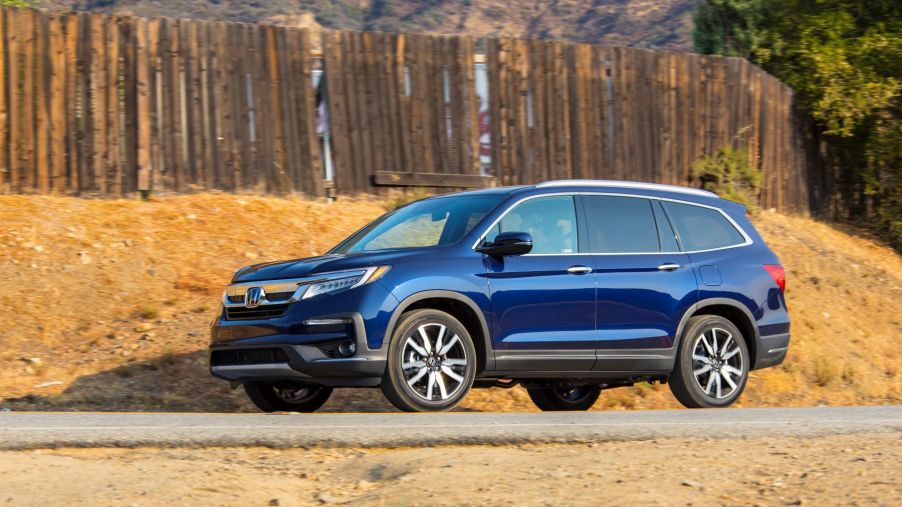 The 2022 Honda Pilot Elite SUV in blue parked in the desert near a wooden fence