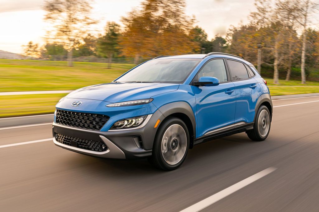 The 2022 Hyundai Kona Limited subcompact SUV in a blue paint color option driving on a frontage highway road, it beats the 2022 Toyota Corolla Cross in most ways