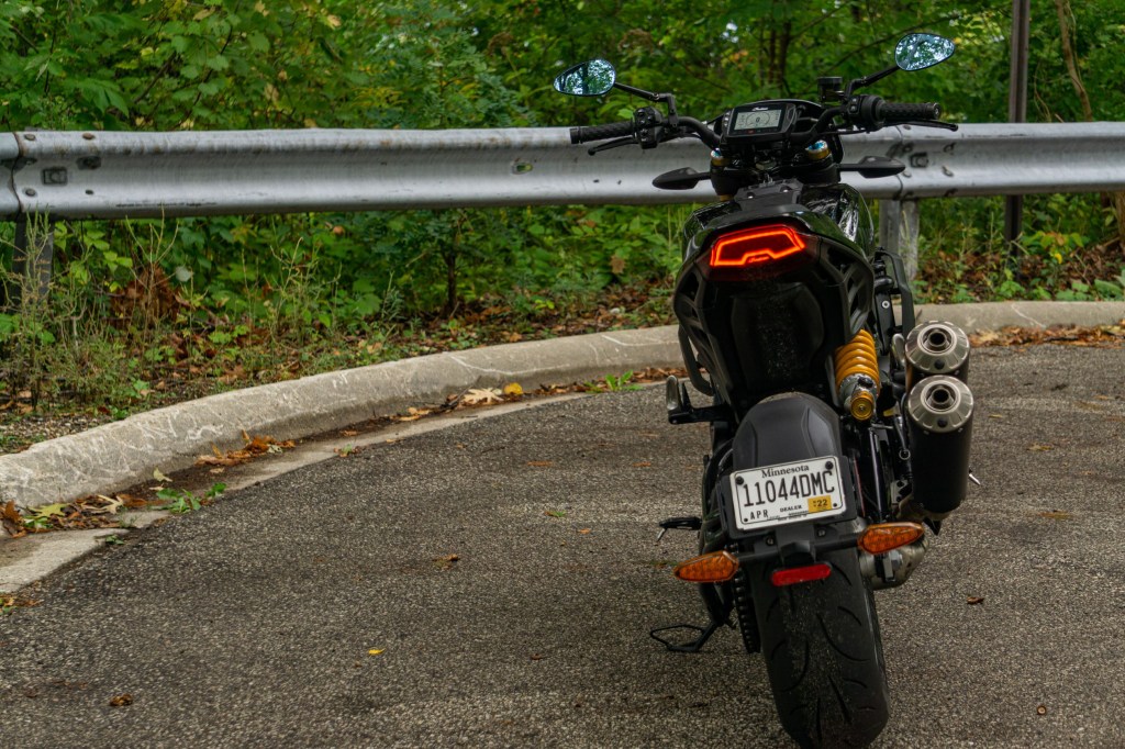 The rear view of an accessorized black 2022 Indian FTR S with its lights on on a forest dead-end road