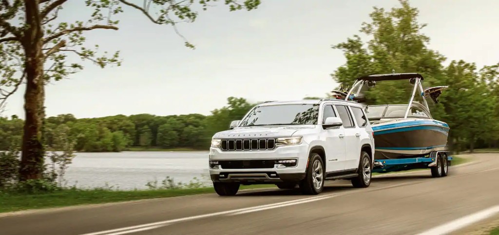 A white 2022 jeep wagoneer tows a boat down the road near water