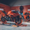 Two orange-and-black 2022 KTM RC 390s with tire warmers on paddock stands in a garage