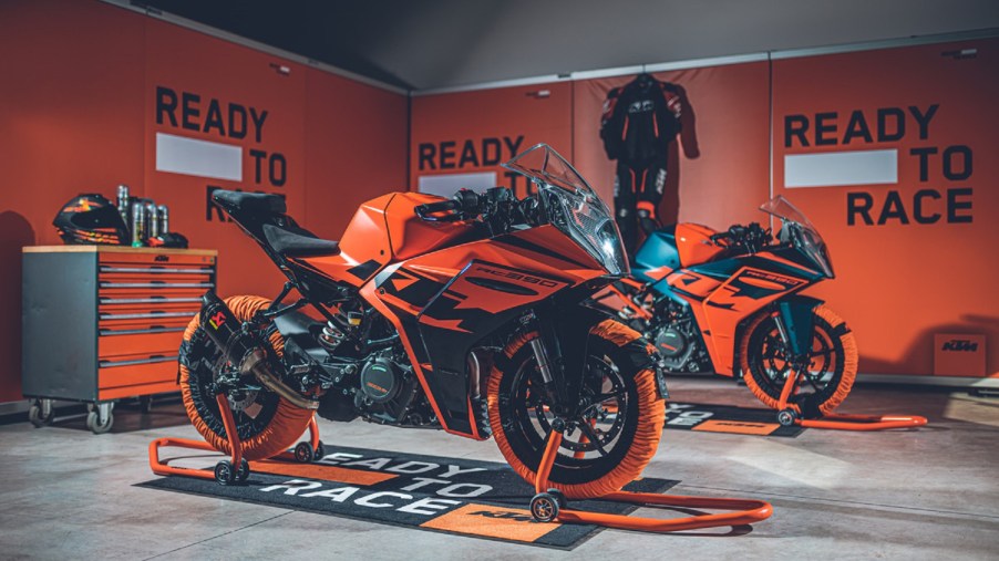 Two orange-and-black 2022 KTM RC 390s with tire warmers on paddock stands in a garage