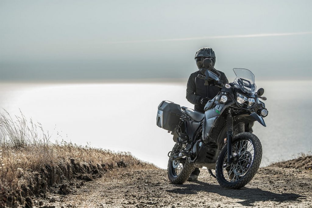 Black-clad rider on a 2022 Kawasaki KLR 650 Adventure gray-camo dual sport motorcycle in the desert