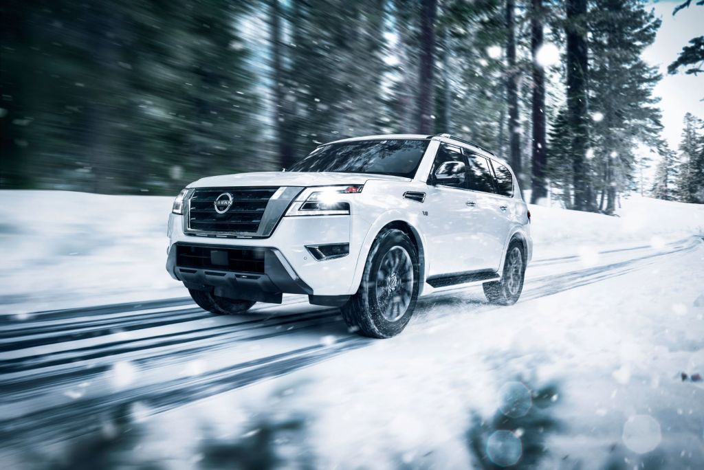 The 2022 Nissan Armada full-size SUV in white driving on a forest road during the winter, avoid this SUV to save money on gas.
