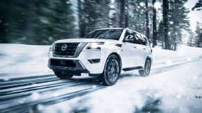The 2022 Nissan Armada full-size SUV in white driving on a forest road during the winter
