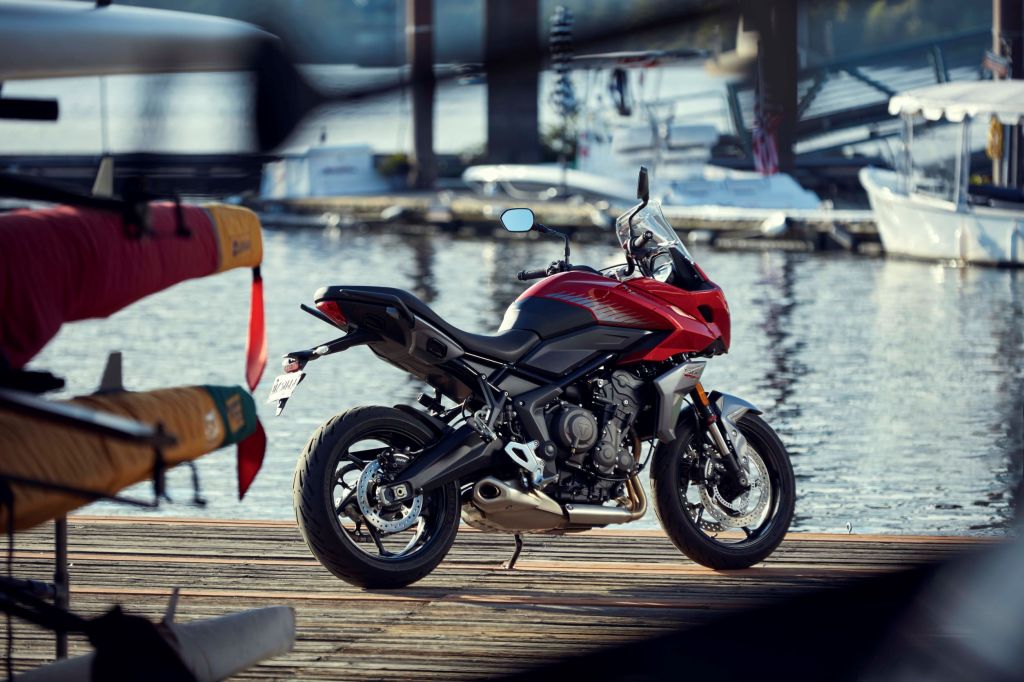 The rear 3/4 view of a red-black-and-silver 2022 Triumph Tiger Sport 660 by some boats on the water