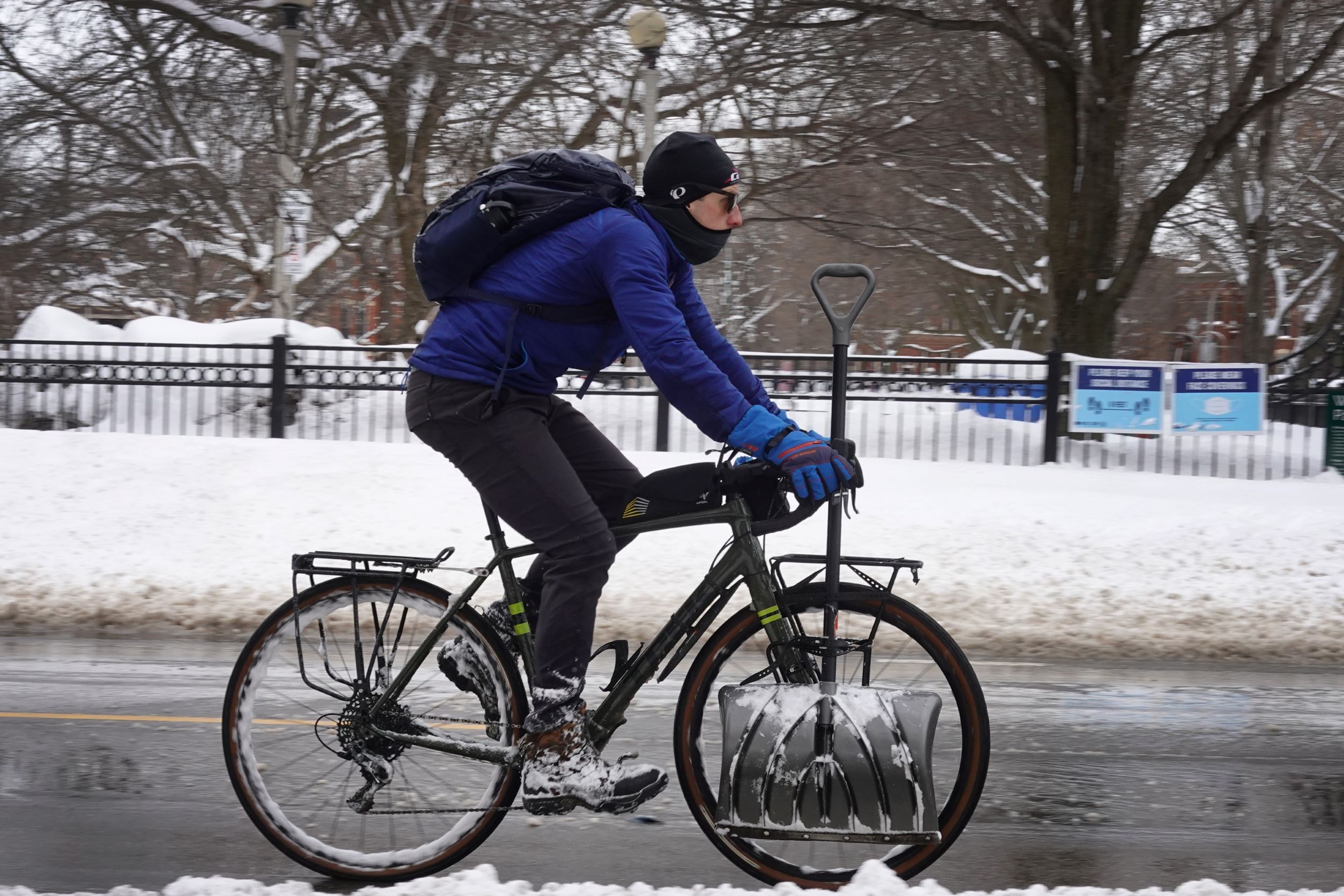 A Chicago cyclist with a shovel rides down the street dressed in winter cycling gear