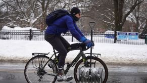 A Chicago cyclist with a shovel rides down the street dressed in winter cycling gear