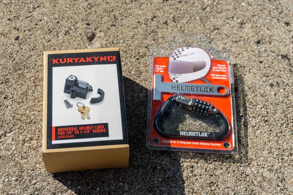 A black Kuryakyn motorcycle helmet lock in its box next to a black Helmetlok lock
