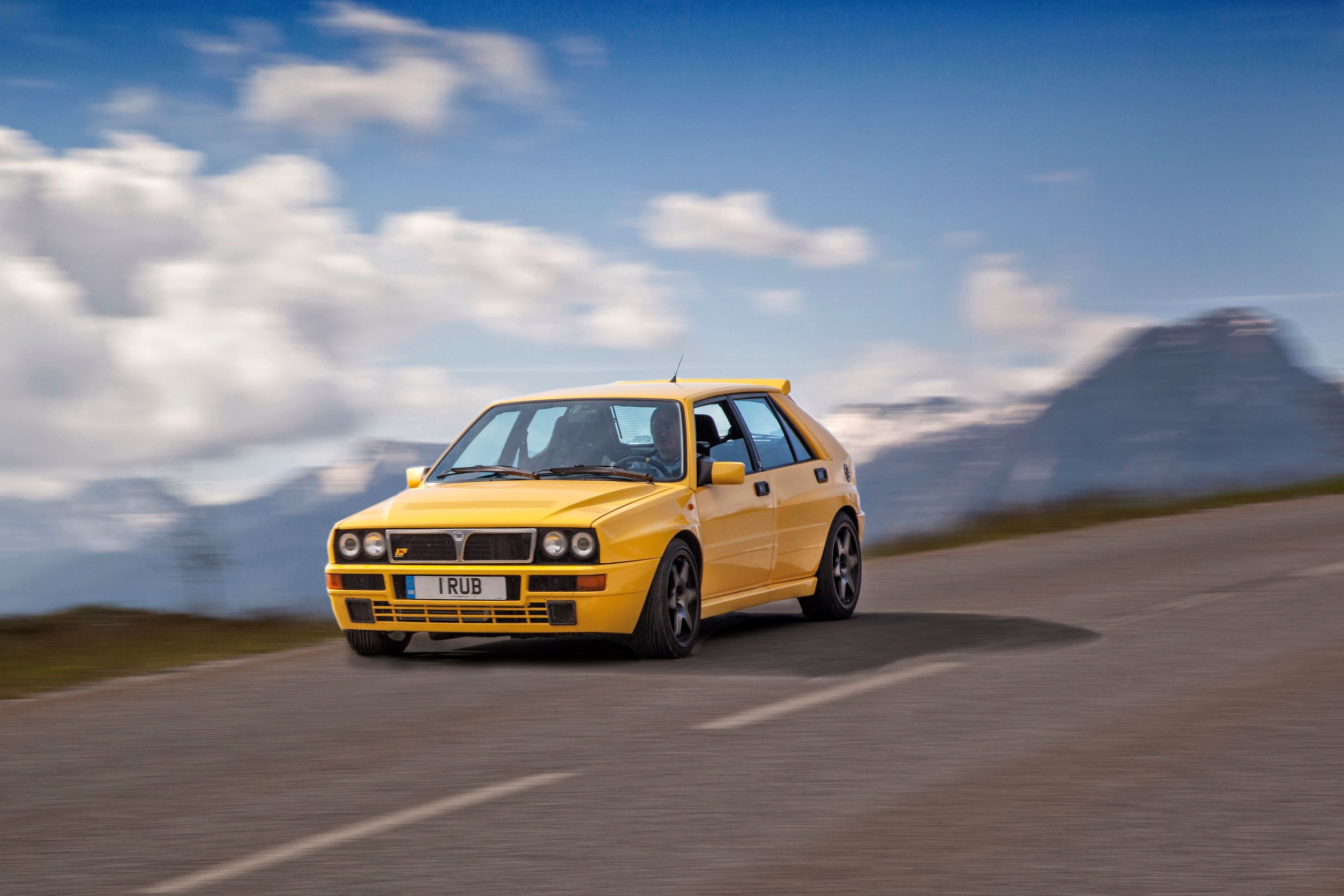 A yellow Lancia Delta Integrale drives through the French Alps
