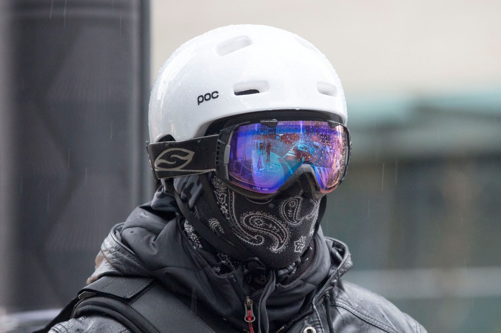A black-clad cyclist wearing blue-tinted goggles and a black face covering for winter cycling
