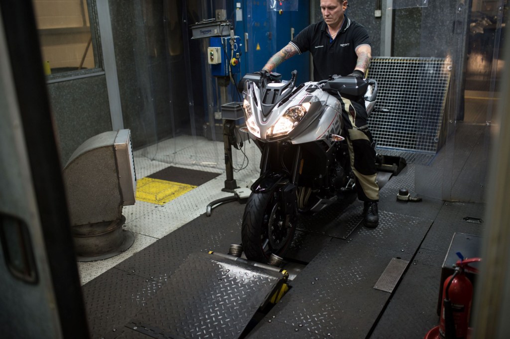 A technician measures a silver-and-gray 2017 Triumph Tiger Sport's horsepower and torque on a motorcycle dyno
