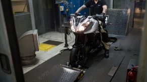 A technician measures a silver-and-gray 2017 Triumph Tiger Sport's horsepower and torque on a motorcycle dyno