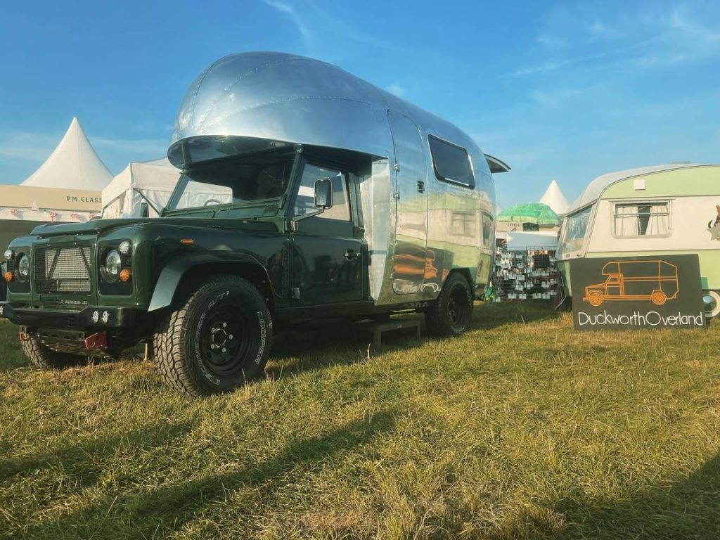 The Duckworth Aerover parked in the grass was built using a Land Rover Defender and a Airstream camper-style camper on the back