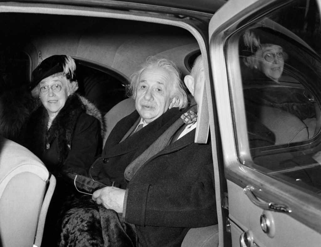 Albert Einstein sitting in a car with his wife and another man, highlighting story of him driving a flying car