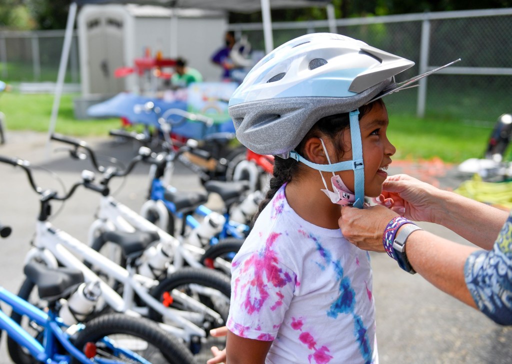An adult helps a child adjust their bicycle helmet